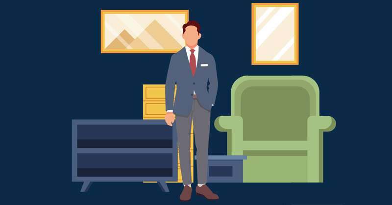 A joiner in a suit standing beside an armchair and a fitted unit